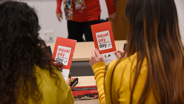 Dos estudiantes universitarias sostienen un tríptico informativo del Equal Pay Day
