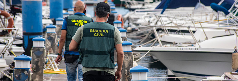 Dos agentes caminan por el Puerto Deportivo locxalizando las embarcaciones a incautar
