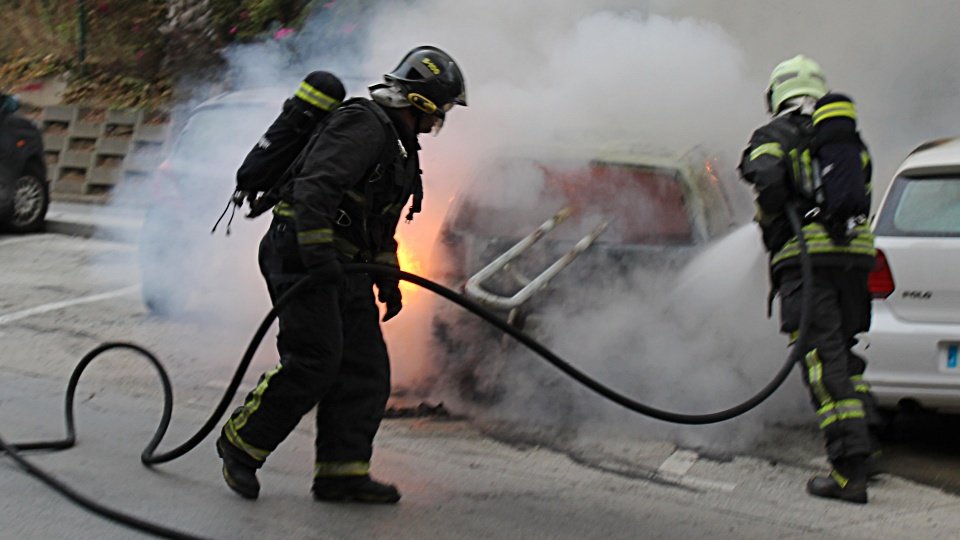 Dos bomberos, apagando las llamas de un coche incendiado