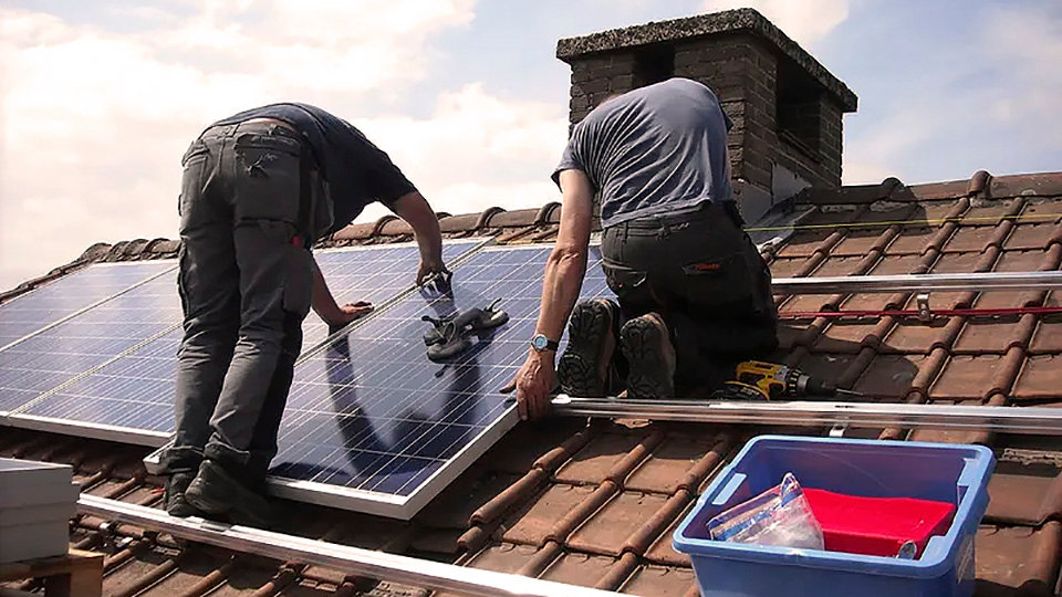 Dos operarios instalan paneles fotovoltaicos en un tejado