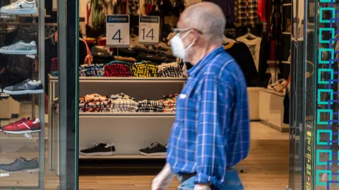 Un hombre con mascarilla pasa frente a una tiemda en el Paseo del Revell&iacute;n