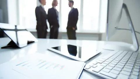 Technological devices and financial document at workplace on background of three businessmen discussing ideas