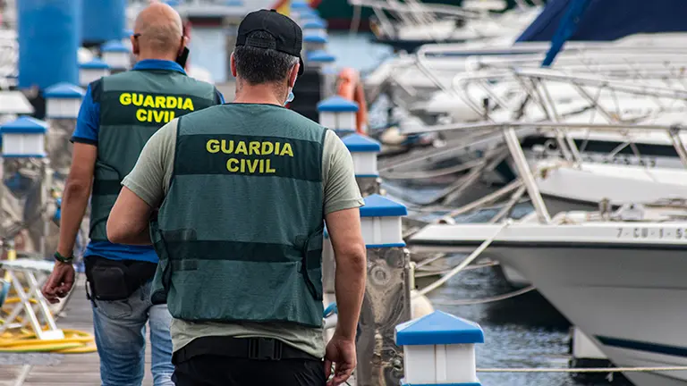 Dos agentes caminan por el Puerto Deportivo locxalizando las embarcaciones a incautar